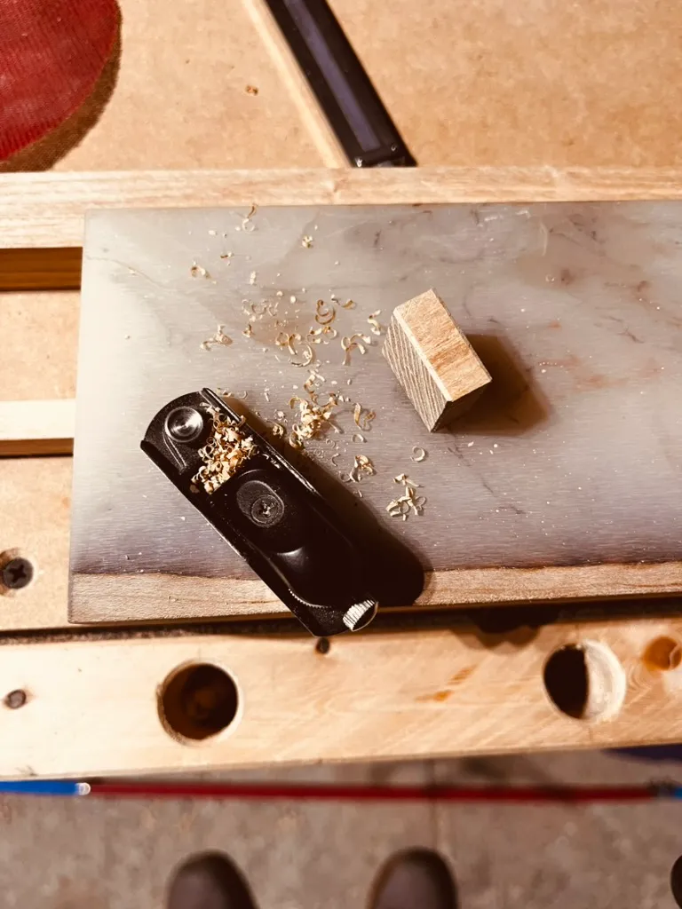 Close-up of a craftsman's hands planing a piece of pale oak